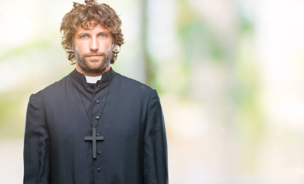 istock Handsome hispanic catholic priest man over isolated background with serious expression on face. Simple and natural looking at the camera. 1127775320