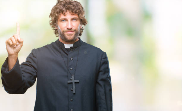 istock Handsome hispanic catholic priest man over isolated background showing and pointing up with finger number one while smiling confident and happy. 1127775338