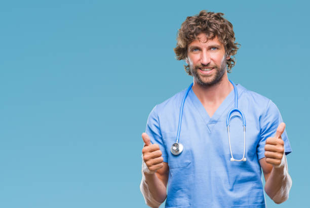istock Handsome hispanic surgeon doctor man over isolated background success sign doing positive gesture with hand, thumbs up smiling and happy. Looking at the camera with cheerful expression, winner gesture. 1127775430