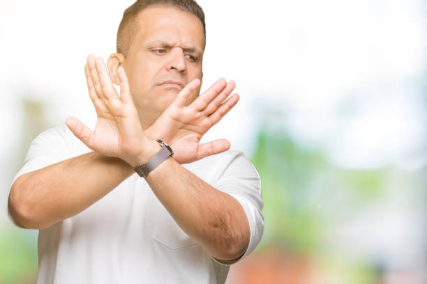 istock Middle age arab man wearig white t-shirt over isolated background Rejection expression crossing arms and palms doing negative sign, angry face 1127775814