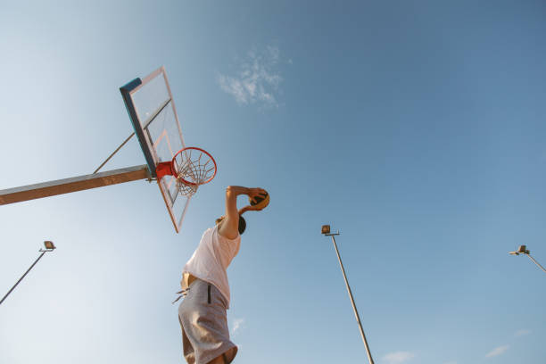 Slam dunking like a professional Low angle view of young athlete slam dunking on hoop, outdoor on day, directly below track and field stadium stock pictures, royalty-free photos & images
