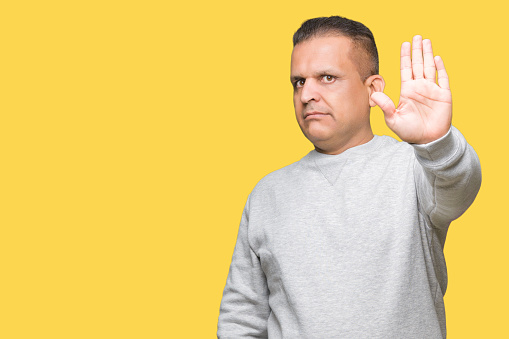 Middle age arab man wearing sport sweatshirt over isolated background doing stop sing with palm of the hand. Warning expression with negative and serious gesture on the face.