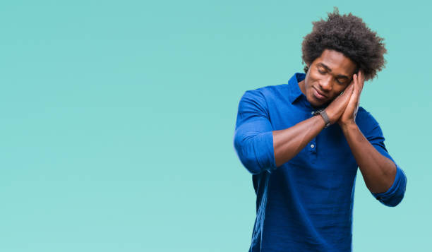 istock Afro american man over isolated background sleeping tired dreaming and posing with hands together while smiling with closed eyes. 1127776509