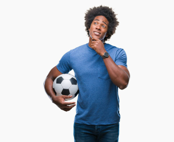 афро американский человек, держащий футбольный мяч над изолированным фоном серьезное лицо думать о вопросе, очень путают идею - football human hand holding american football стоковые фото и изображения