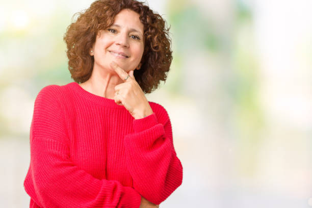 美しいミドルエージャーシニア女性赤い冬のセータークロス腕と手で顎に提起された笑顔でカメラに自信を持って孤立した背景の上に。前向きに考える。 - front view female isolated on red happiness ストックフォトと画像