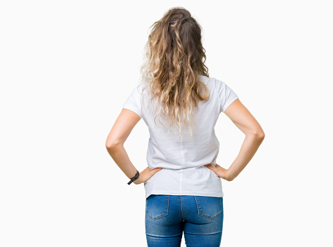 Beautiful young blonde woman wearing glasses over isolated background standing backwards looking away with arms on body