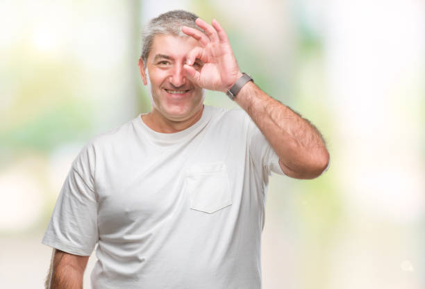 istock Handsome senior man over isolated background doing ok gesture with hand smiling, eye looking through fingers with happy face. 1127786460