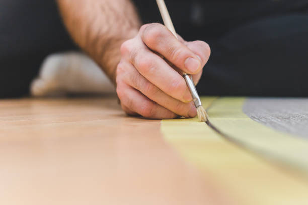 istock Worker with a brush applies a primer in the joint between tile and parquet 1127794542
