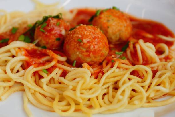 yellow boiled spaghetti with red sauce and round meatballs on a white plate