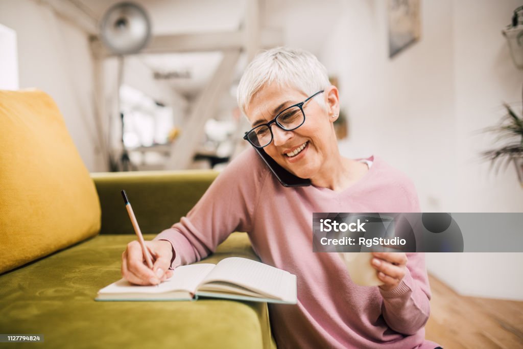 Happy woman talking on phone Woman talking on mobile phone and writing Using Phone Stock Photo