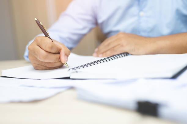 istock close up hand young man are sitting using pen writing Record Lecture note pad into the book on the table wood. 1127797175