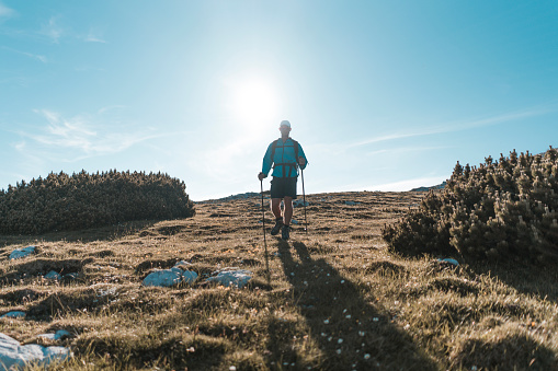 Young man in a silhouette with a backpack hiking in the mountains. Exploring in the nature on a warm sunny day.