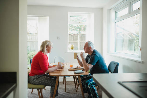 Mature Couple Enjoying Breakfast at Home Mature couple are having breakfast together at the dining table in their home. old man pajamas photos stock pictures, royalty-free photos & images