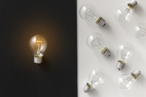 Idea, leadership and creativity concept. Illuminated lamp bulb separated from other, contrast white and black background