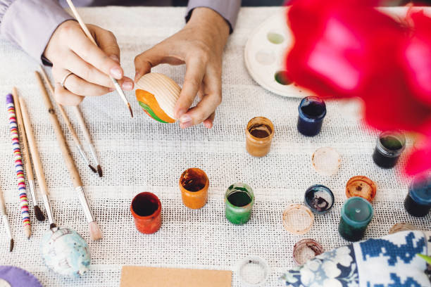 istock Happy Easter concept, flat lay. Hands holding and painting easter egg on rustic table with paint,brushes, tulips bouquet, space for text. Child decorating easter egg, holiday preparations 1127805882