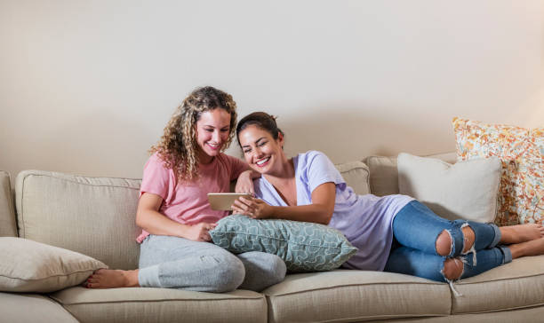 istock Hispanic sisters on sofa looking at mobile phone 1127805944