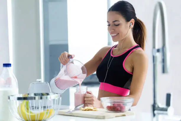 Shot of sporty young woman serving strawberry smoothie in a glass jar in the kitchen at home.