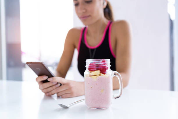 strawberry and banana smoothie. in the background, sporty young woman using her mobile phone. - blueberry fruit berry berry fruit imagens e fotografias de stock