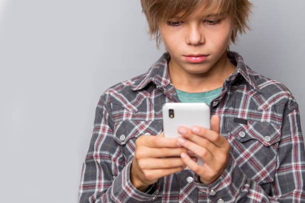 istock Cute teenage boy using cellphone isolated over grey background, focus on phone 1127807674