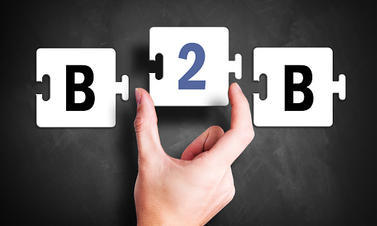hand holding a puzzle piece forming the connection of B2B in front of a blackboard