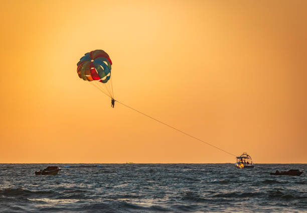 amazing shot at sunset of Parasailing water amusement Indian water sports in north Goa  flying on a parachute behind a boat on a summer holiday by the sea in the resort Baga beach Goa India parasailing stock pictures, royalty-free photos & images