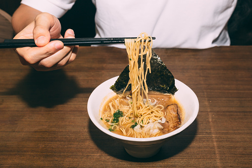 Hand pinching Hakata style Shio Chashumen (Salt soup) with chopsticks including noodle, sliced barbecued pork, sprout, seaweed and scallion.