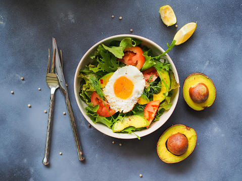 Avocado salad bowl with fried egg on top in topview for diet food or healthy eating concept.