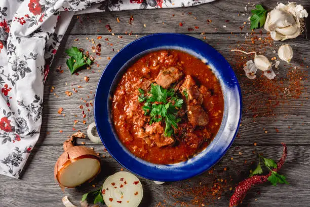 Stewed veal meat with spices in a tomato sauce, veal meat in tomato sauce with onion, garlic, chili pepper on the wooden background. boiled meat and fresh tomato top view, flat lay