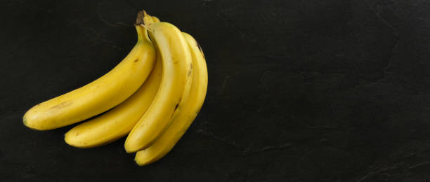 istock Top view, bunch of bananas on black stone board. Banner with copy space for text on right. 1127823842