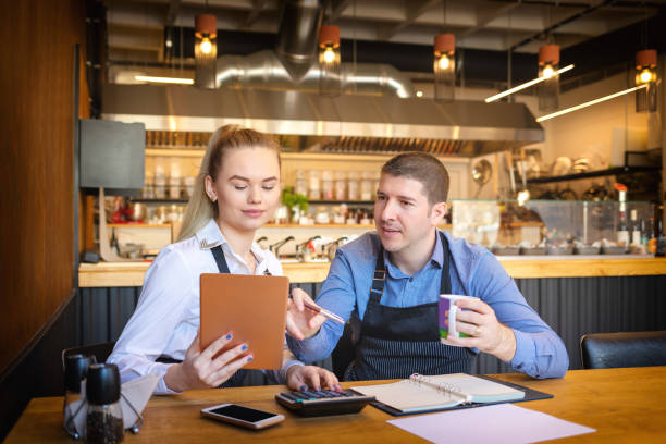 jovem e mulher passando por papelada junto em seu restaurante. proprietários do restaurante família pequena discutir finanças calcular as contas e despesas da sua empresa de pequena porte. - fast food restaurant restaurant cafe indoors - fotografias e filmes do acervo