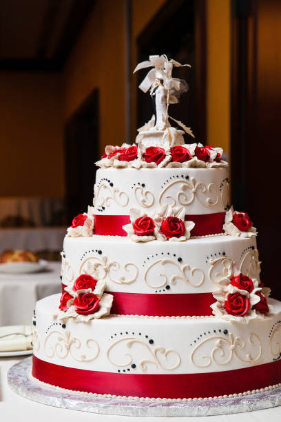 weiße hochzeitstorte mit roten fondant blumen und roten bändern auf jede schicht puderzucker - rote hochzeitstorten stock-fotos und bilder