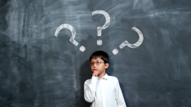 Schoolboy Thinking Hard by Chalkboard with Question Marks