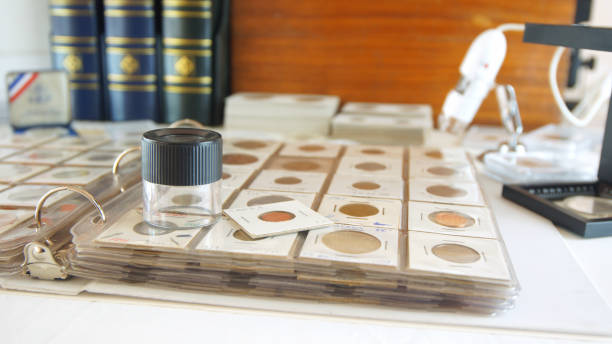 Round magnifying glass on album with coins from different countries Round magnifying glass on album with coins from different countries - Numismatic scene coin collection stock pictures, royalty-free photos & images