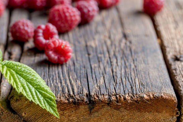 istock Ripe, freshly picked raspberries with leaves, on rustic wooden old table surface. 1127833521