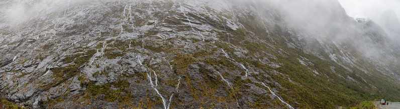 A panoramic showing mountain walls around the exit to the Homer Tunnel, also including a lookout area in the bottom right.