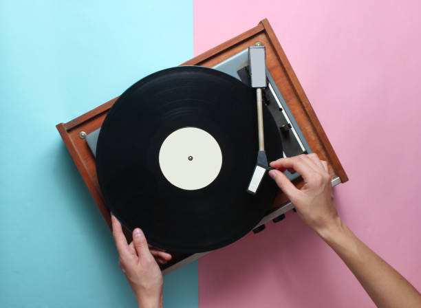 istock Female hands  use retro vinyl player on a blue pink pastel background. DJ. Top View 1127836795
