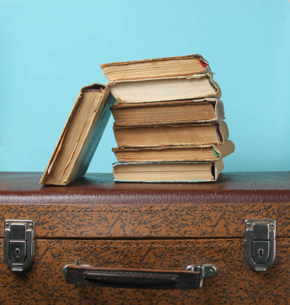 istock Stack of old books on retro suitcase on a blue background 1127836828