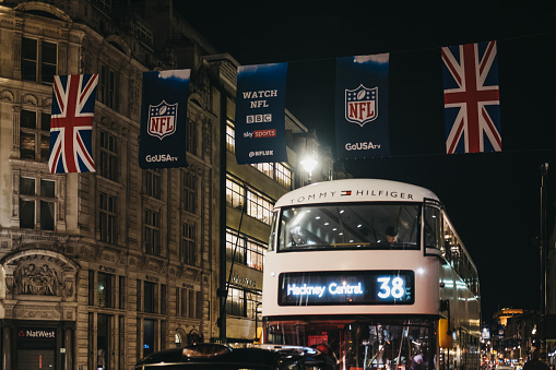 London, UK - December 17, 2018: Black taxi and bus on Regent Street, London, in the evening. The street is decorated with NFL flags to celebrate the event and NFL games played in the capital in 2018.