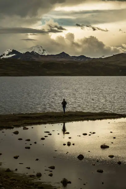 The young woman is reflected in the golden lake. With the Andes mountains in the distance showing a dramatic sky.