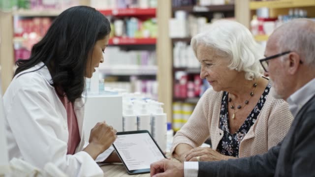 Pharmacist discussing with couple on digital tablet