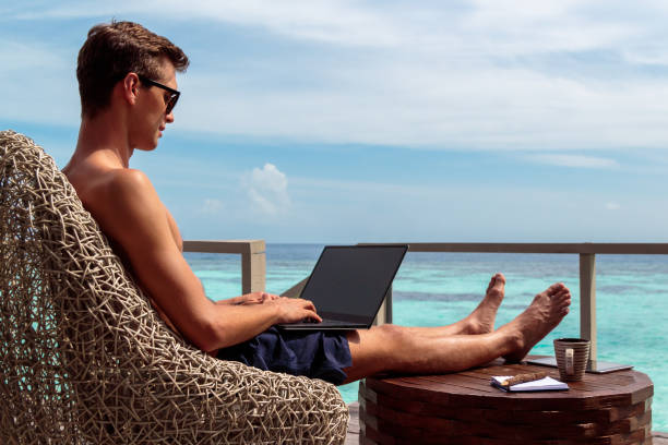 istock young man in swimsuit working on a laptop in a tropical destination 1127857574