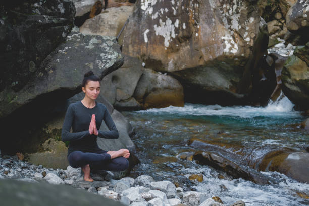 istock Young slim woman practicing yoga outdoors on stone shore of mountain river. Unity with nature concept. Girl sitting on tiptoes 1127865621