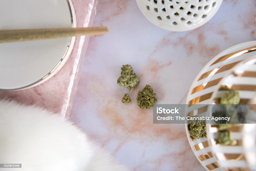 Marijuana Joint on Tray, Buds on Pink Marble Vanity Luxury Cannabis Top down, close up view of cannabis buds on a pink marble vanity with a marijuana joint on a tray. Gold and white jewelry tray adorned with cannabis buds. Vanity contains pink velvet and white fur. Ashtray Stock Photo