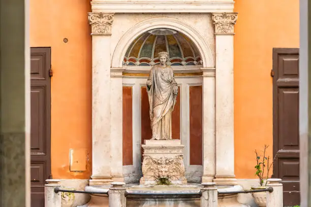 City alley and entrance to Palazzo Ferrajoli with sculpture statue water fountain and orange wall in Rome, Italy