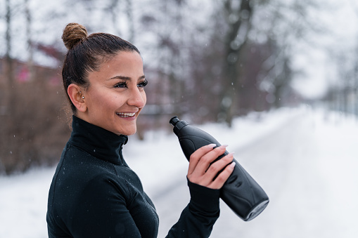 Two women are out in the snow on a cold winter day in Sweden, exercising together by jogging in the city. Drinking from a bottle of water.