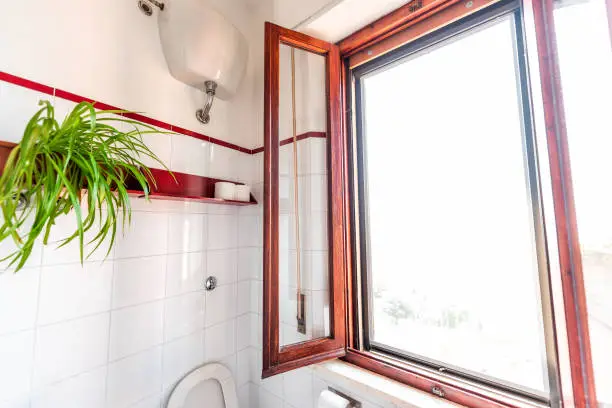 White clean toilet bathroom with red color wooden window frame tiles tiled wall in Italian style apartment villa home house in Tuscany, Italy