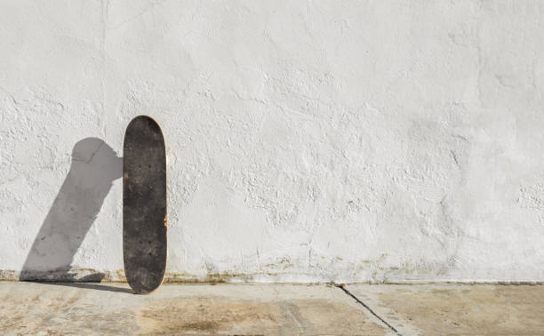 Skateboard on deteriorated white wall during a sunny afternoon with big copy space. Skateboarding background, street sport.