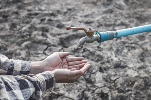 Hand taking fresh water and Lake dried with empty land full of crakced earth and the man standing on behide metaphor water scarcity and climate change impact.
