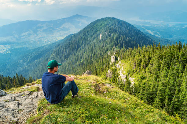 Stock photograph of an adult caucasian man looking at view and contemplating in the landmark Ceahlau Massif, Carpathians, Romania.
