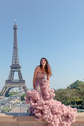 Beautiful hipster girl dressed to impress in a pastel pink ballroom dress with Eiffel Tower in background